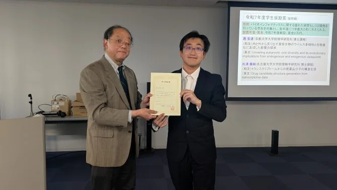 Hongda Zhao and an award presenter hold the FY2025 Bioinformatics Japan Student Encouragement Award certificate.